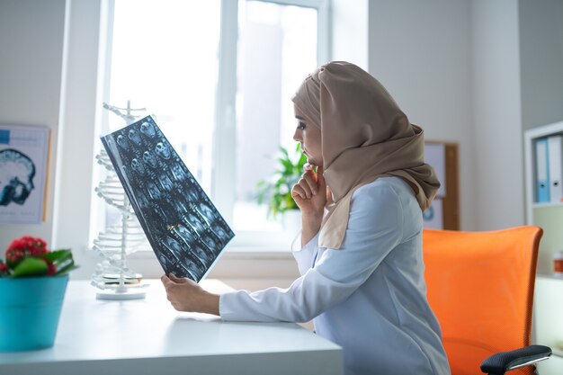 Docteur assis. Femme médecin intelligente portant un uniforme blanc et un foulard assis à la table de travail