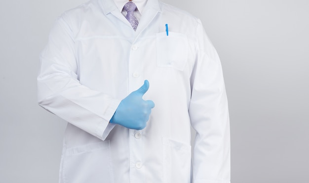 Photo docteur en blouse blanche et cravate montre avec sa main un geste comme, portant des gants médicaux en latex bleu