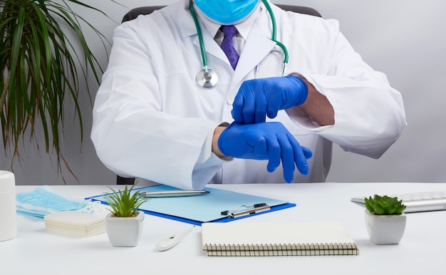 Docteur en blouse médicale blanche est assis à une table dans une chaise en cuir marron et met des gants médicaux stériles