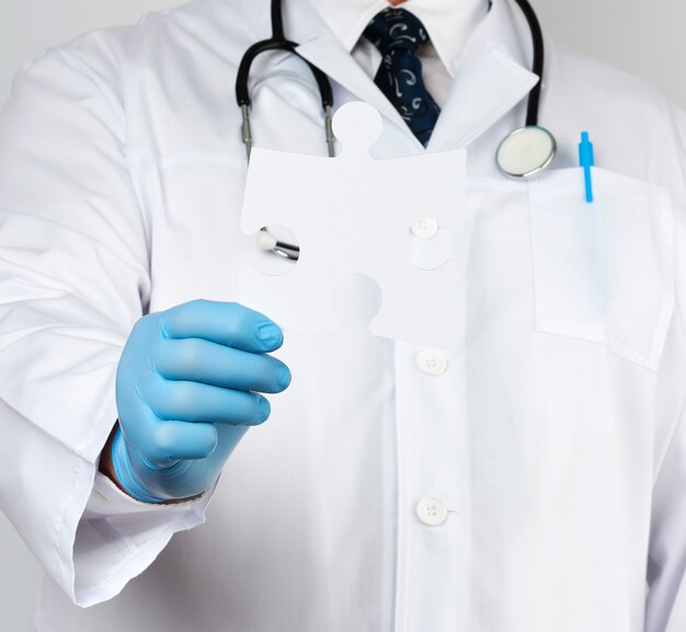 Photo docteur en blouse médicale blanche et gants en caoutchouc bleu tient un puzzle en papier blanc