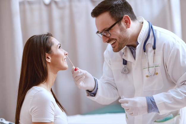 Docteur caucasien souriant prenant un écouvillon du nez de son patient. Intérieur de la clinique.