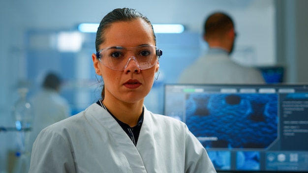 Photo docteur chimiste fatigué regardant la caméra en soupirant dans un laboratoire moderne équipé. équipe multiethnique examinant l'évolution du virus à l'aide d'outils de haute technologie et de chimie pour la recherche scientifique et le développement de vaccins.