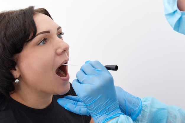 Docteur dans une combinaison de protection prenant un écouvillonnage de gorge et de nez d'un patient pour tester d'éventuelles