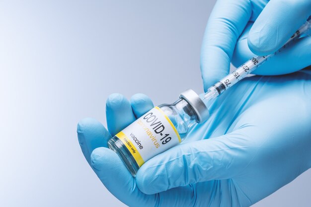 Le docteur dans les gants bleus de latex remplissent la seringue avec le vaccin du flacon en verre