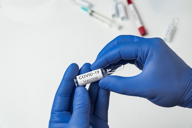 Docteur détient une ampoule avec étiquette Covid-19 sur fond blanc. vaccin contre la grippe contre le coronavirus