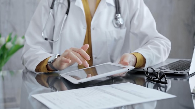 Docteur femme utilisant la tablette sur le bureau en verre dans le bureau médical médecine et soins de santé