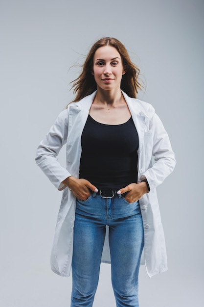 Docteur gai moderne dans un manteau blanc sur un fond gris Femme médecin avec un sourire sur son visage