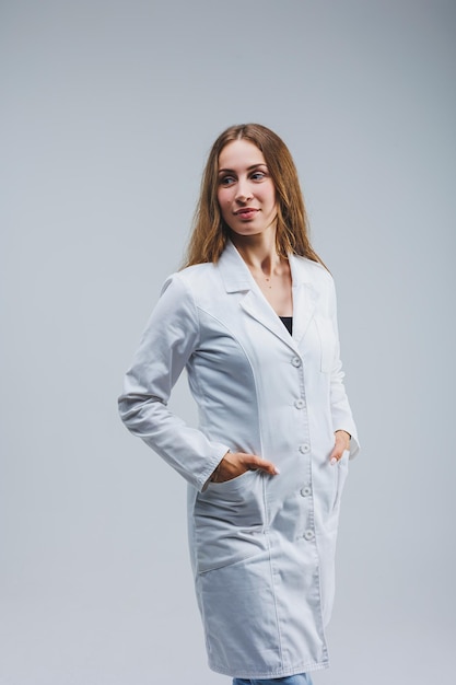 Docteur gai moderne dans un manteau blanc sur un fond gris Femme médecin avec un sourire sur son visage