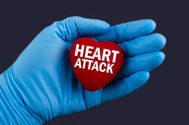 Docteur en gants bleus tient un coeur avec texte crise cardiaque, concept.