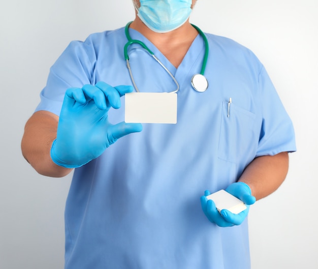 Docteur en gants en latex stériles et uniforme bleu est titulaire d'une carte de visite blanche vierge