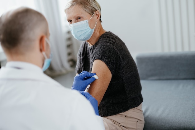 Docteur en gants de protection vaccinant une dame mûre