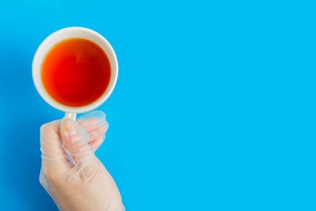 Docteur main dans un gant médical détient la vue de dessus de tasse de thé blanc avec copyspace sur fond bleu