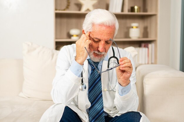 Docteur masculin âgé triste et fatigué en uniforme médical à l'hôpital ou au cabinet du médecin général malheureux