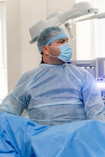 Docteur en masque, gommages et gants en latex. Chirurgien effectuant une opération chirurgicale dans une salle de chirurgie moderne et lumineuse sur fond.