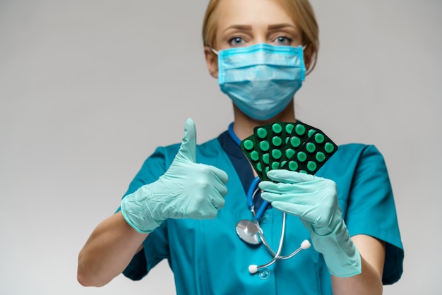 Docteur en médecine infirmière femme portant un masque de protection et des gants en caoutchouc ou en latex - tenant des ampoules de pilules