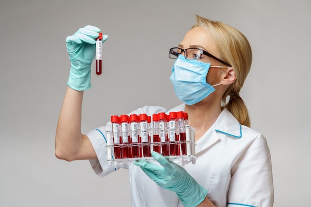 Docteur en médecine infirmière femme portant un masque de protection et des gants - holding rack avec des tests sanguins de virus