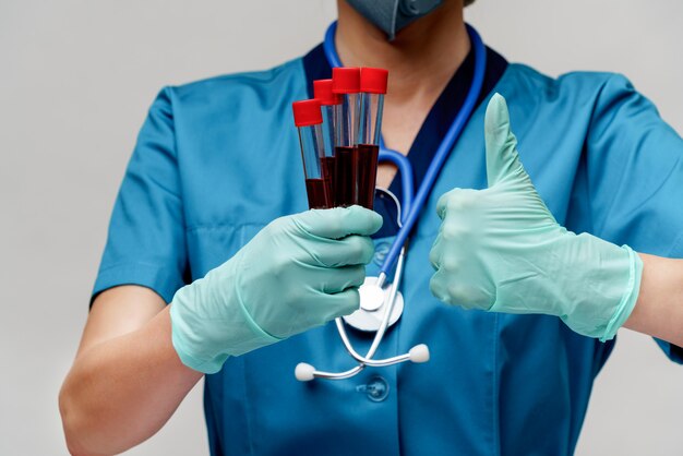 Docteur en médecine infirmière femme portant un masque de protection et des gants - tenant le tube à essai de sang de virus