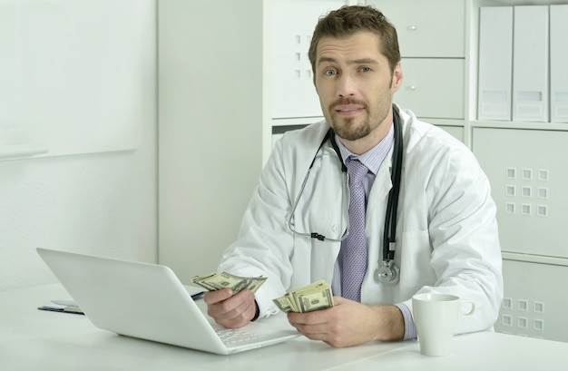 Docteur en médecine travaillant avec un ordinateur portable et de l'argent au bureau