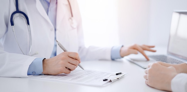 Photo docteur et patient discutent de quelque chose et utilisent un ordinateur portable tout en étant assis l'un en face de l'autre au bureau dans le bureau de la clinique concept de service médical et de médecine parfait