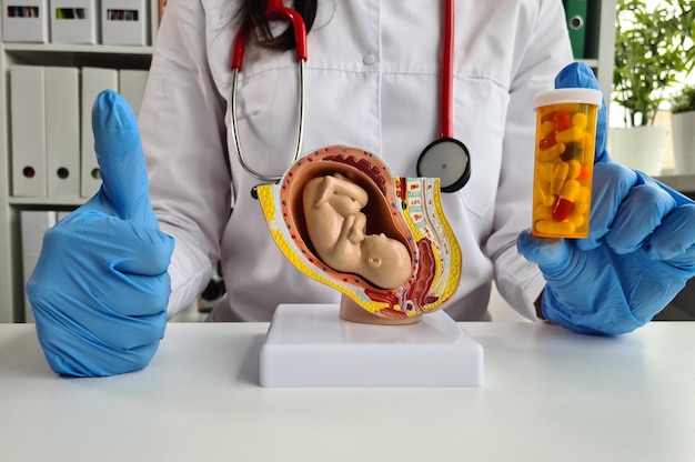 Docteur tenant un modèle de fœtus imprimé en 3D et des pilules dans les mains avec les pouces en l'air.