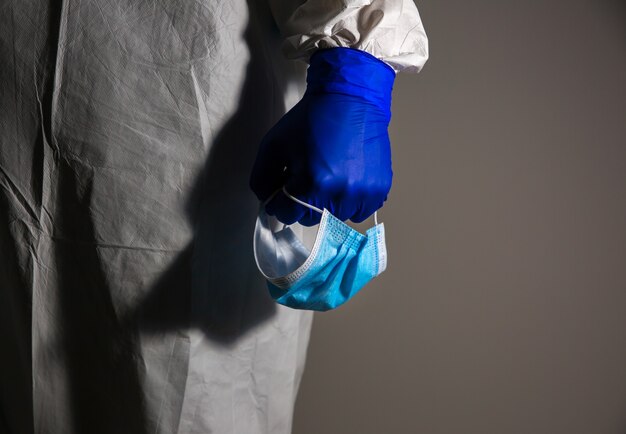 Docteur en tenue de protection médicale et gants, tenant le masque à la main. La fin de la pandémie de virus. Mers de protection par épidémie de virus. Coronavirus (COVID-19). Concept de soins de santé.