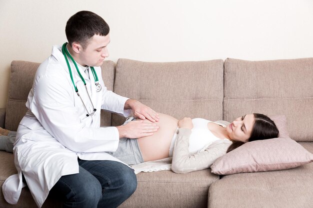 Le docteur touche et examine le ventre d'une femme enceinte à la maison.