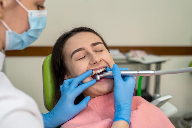 Le docteur traite les dents de sa jeune femme avec une perceuse dentaire dans un cabinet dentaire moderne.