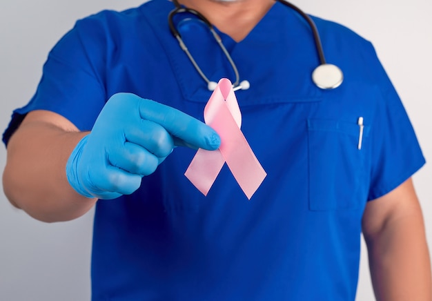 Docteur en uniforme bleu et gants en latex stériles avec un ruban rose, symbole de la lutte contre le cancer du sein