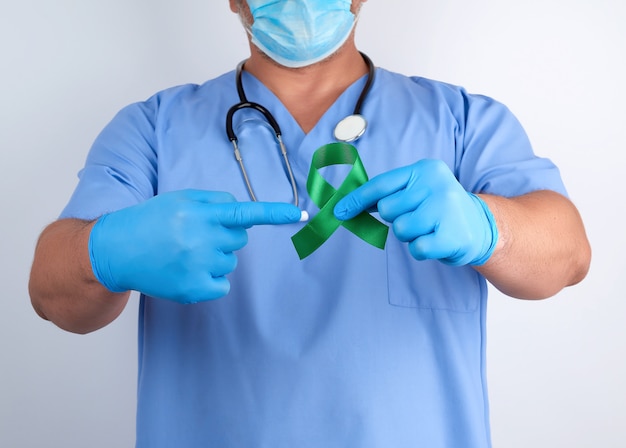 Docteur en uniforme bleu et gants en latex, titulaire d'un ruban vert, symbole des premières recherches