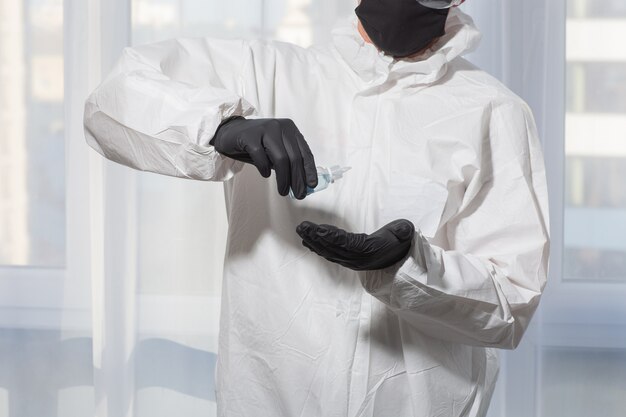 Photo docteur en uniforme de costume epi et gants traite les mains avec un antiseptique. épidémie de coronavirus. concept de mise en quarantaine covid-19. médecin et soins médicaux. équipement de protection individuelle arrêtez le virus.