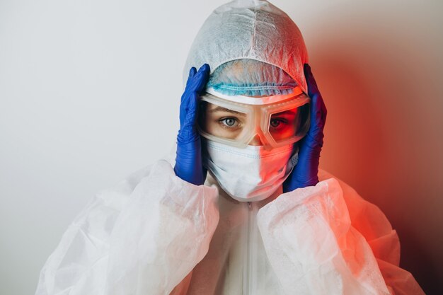 Docteur en uniforme de protection, lunettes, gants sur fond bleu en néon. portrait de gros plan d'un médecin en néon rouge. un homme fatigué se bat contre un coronavirus. COVID 19