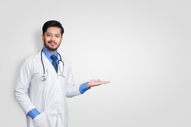 Docteur en uniforme souriant tout en présentant et en pointant isolé sur un mur blanc avec espace de copie