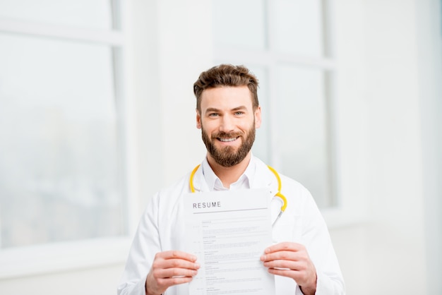 Docteur en uniforme tenant un curriculum vitae pour l'embauche dans l'intérieur blanc