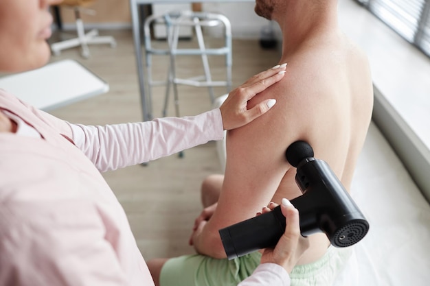 Docteur utilisant un masseur dans une procédure médicale avec un patient elle masse son dos douloureux