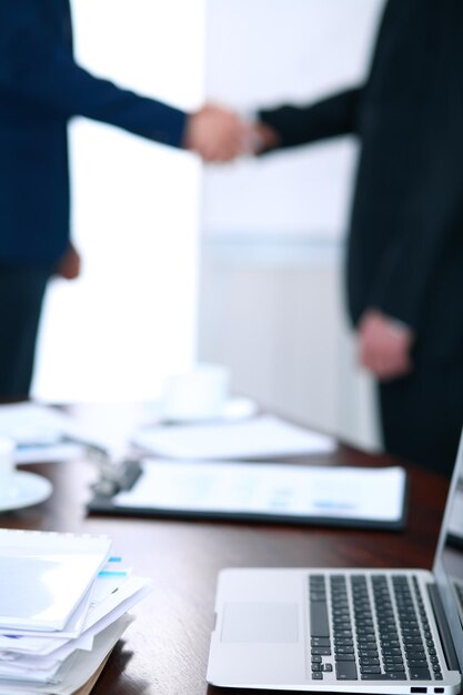 Documents et ordinateur portable sur la table. Gens d'affaires se serrant la main sur le fond.