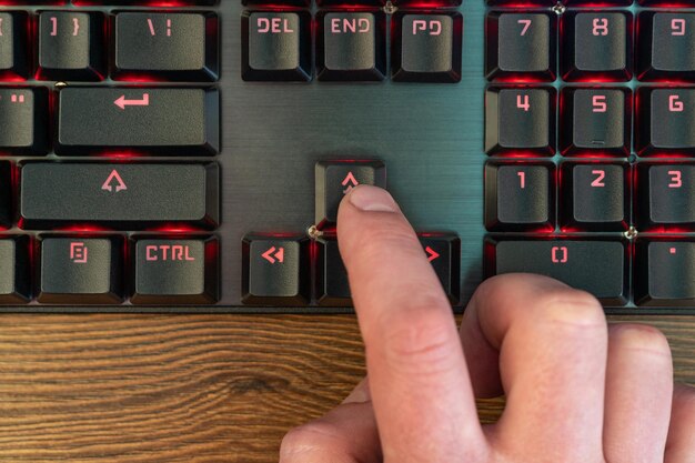 Photo le doigt de la main de l'homme appuie sur la flèche vers le haut du clavier allongé sur une table en bois, gros plan