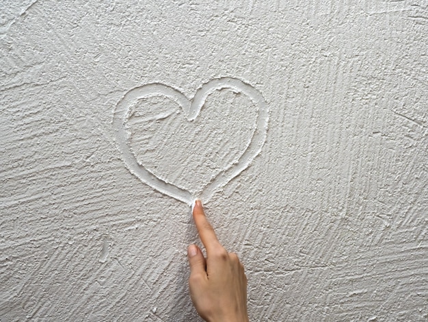 Le doigt peint un cœur sur un mur de stuc blanc. Concept de la Saint-Valentin.