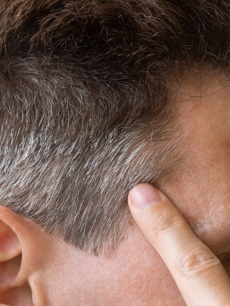 Un doigt pointant vers les cheveux gris sur sa tête.