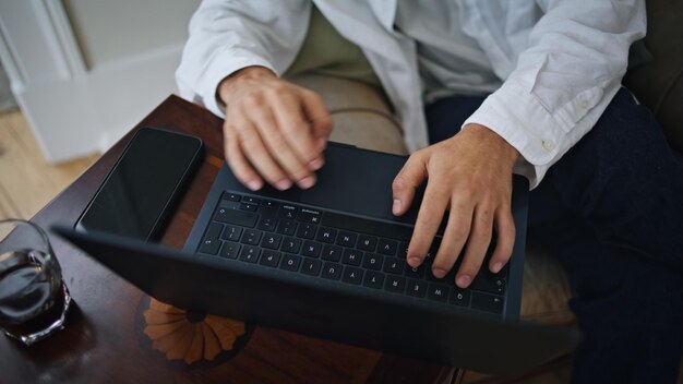 Photo des doigts d'homme travaillant sur un ordinateur à la maison, un gros plan, des mains occupées, un ordinateur portable en train de texter.