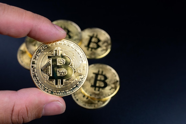 Doigts humains tenant des bitcoins sur fond noir