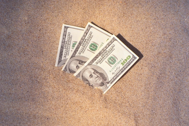 Dolars d'argent à moitié recouverts de sable se trouvent sur la plage gros plan trois cents dollars enfouis dans le sable sur la mer