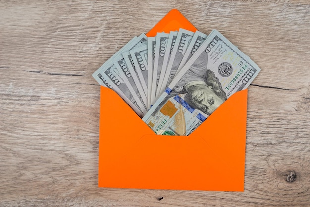 Des dollars dans une enveloppe orange sur la table.