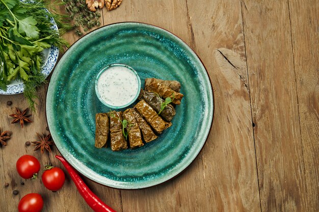 Photo dolma géorgien traditionnel - riz avec de la viande hachée dans des feuilles de vigne sur une plaque bleue avec une sauce au yogourt. surface en bois. vue de dessus. sarma