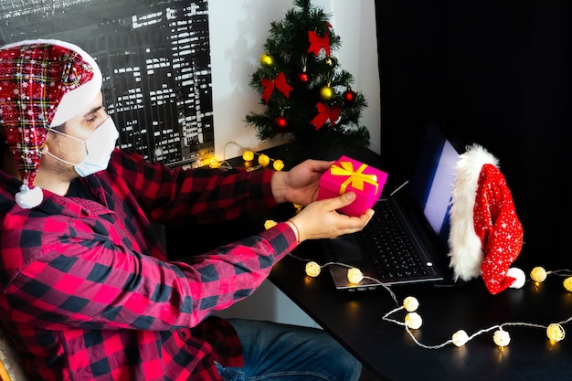 Don de cadeaux de Noël. Homme partageant des cadeaux par le biais d'appels vidéo. Vacances dans l'isolement. Arbre du nouvel an et lumières avec décorations. Famille et amis célébrant en ligne.