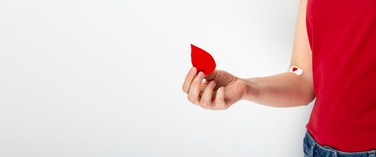 Photo don de sang. jeune fille en t-shirt rouge tient goutte dans sa main, seconde main enregistrée avec patch avec coeur rouge après avoir donné du sang sur fond gris.