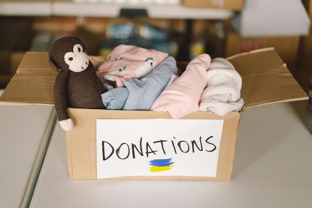 Don de vêtements pour les réfugiés d'Ukraine soutien aux victimes de la guerre aidant les gens à faire don d'une boîte avec le drapeau ukrainien Concept d'aide humanitaire