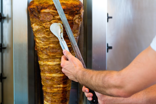 Doner kebab - vendeur sympathique dans un restaurant de restauration rapide turque, couper la viande avec un couteau bien aiguisé en face de brochette