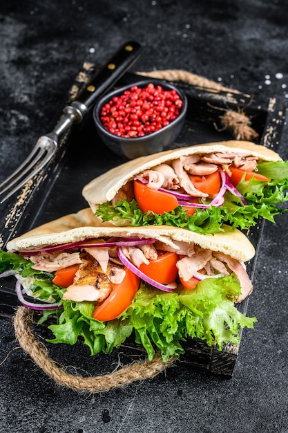 Doner kebab avec viande de poulet grillée et légumes dans du pain pita sur un plateau en bois.