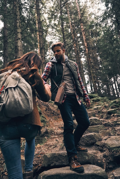 Donner un coup de main. Jeune couple se tenant la main et se déplaçant vers le haut lors d'une randonnée ensemble dans les bois