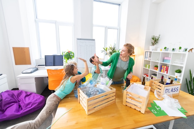 Donner un high five. Professeur aux cheveux blonds cool moderne donnant cinq à ses élèves après le tri des déchets